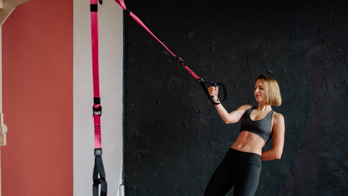 Fit woman performing workout with suspension trainer in gym. Strength and balance exercise indoors.